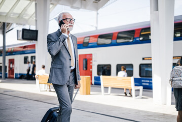 Senior businessman talking on smart phone while walking at subway or train platform.
