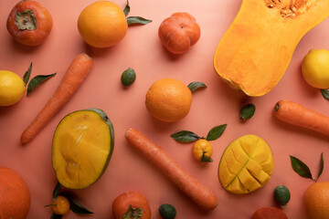 Ripe and tasty orange and yellow fruits, carrots and pumpkin around coral color background. flat lay