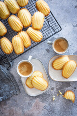 Freshly made madeleines on a cooling rack with two cups of coffee in front with serving trays