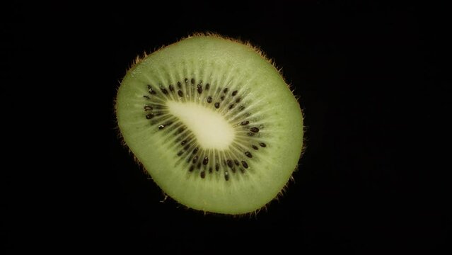 The cut half of the kiwi rotates on a black background. Close-up.