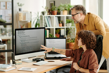 Young confident programmer pointing at data on computer screen while brainstorming and discussing...