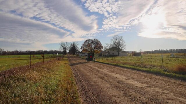 Amish horse and buggy with horse at near run, on rural, dirt road, with beautiful clouds in the blue sky.