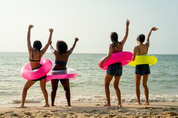 Four of teen girls with pink and yellow swimming ring look at the sea and enjoy with dancing together on the beach during holiday or vacation.