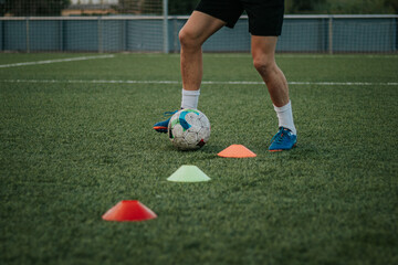 Vertical shot of player's legs dribbling cones on grass field. © David Gari
