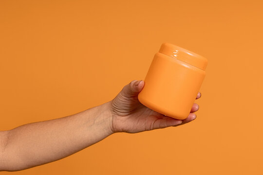 a female hand holds out an opaque plastic yellow jar on a yellow background