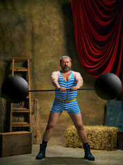 Vintage portrait of retro circus strongman wearing blue striped sports swimsuit training with...