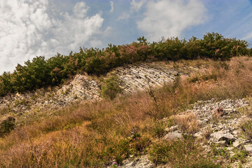 The slope of the mountain against the sky. Beautiful picturesque yellow mountainside against a blue cloudy sky. A rocky mountain slope with dry vegetation on a sunny autumn day.