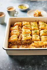 Side view of walnut baklava with delicious pistachio topping, honey and served with coffee on the side.