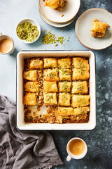 Tray of homemade walnut baklava, cut into squares and topped with chopped pistachios, served with cups of coffee. Traditional Middle Eastern dessert with flaky phyllo pastry, nuts, and honey syrup.