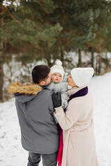 Family walking in the snow having fun in winter park on a bright day hugging each other and smiling