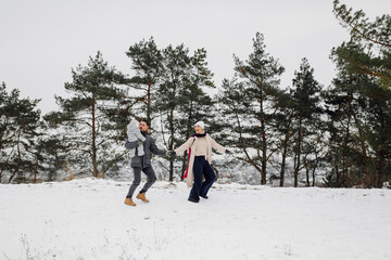Family walking in the snow having fun in winter park on a bright day hugging each other and smiling