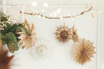 Stylish paper christmas stars and lights hanging on white wall background. Scandinavian festive...