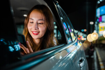 Asian businesswoman commuting from office in Taxi backseat with mobile phone on road in city at night after late work, Beautiful woman using smartphone sitting back seat her car in urban