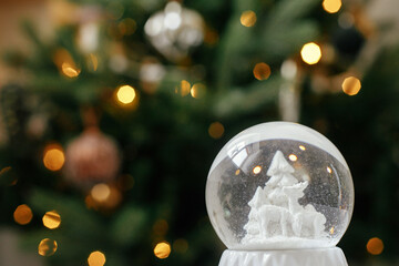Stylish christmas snow globe on background of christmas tree in lights in festive decorated boho...