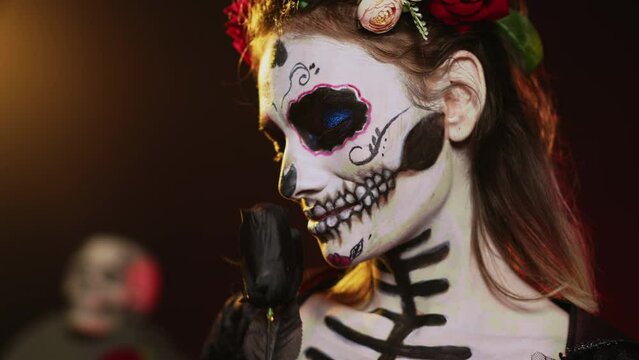 Glamorous goddess wearing death costume and flowers wreath over studio background, acting like holy santa muerte. La cavalera catrina lady of dead with skull body art, mexican culture. Handheld shot.