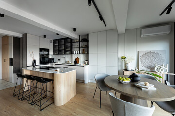 Modern composition of kitchen space with design kitchen island, black hookers, grey table, flowers, furnitures, big window and elegant personal accessories. Stylish home decor. Template