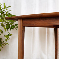 Mid-century modern dark walnut wood dining table. Corner view of vintage tapered-leg table before white curtains and green hosueplants. 
