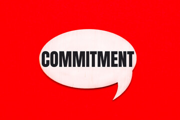 On a bright red background, a light wooden curly card with the text COMMITMENT