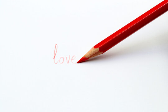 Red pencil drawing the word love on a sheet of paper