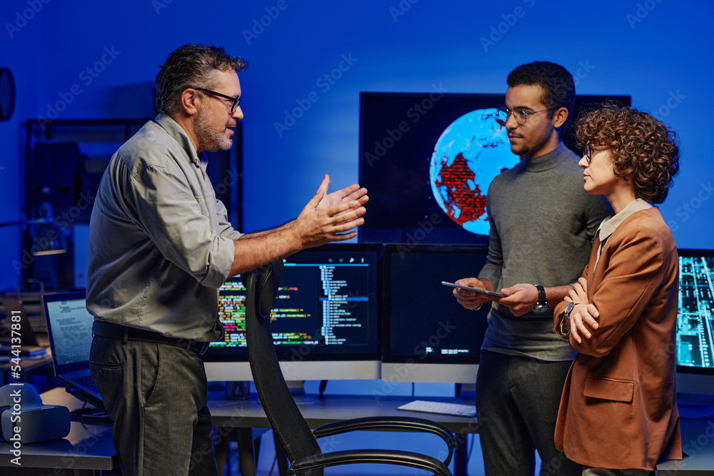 Aufkleber Side view of confident mature boss giving working instructions to young subordinates standing in front of him at meeting in server room