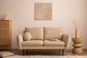 Creative composition of living room interior with mock up poster frame, beige sofa, round wooden coffee table, vase with dried flowers, bright rug, rattan commode and personal accessories. Home decor