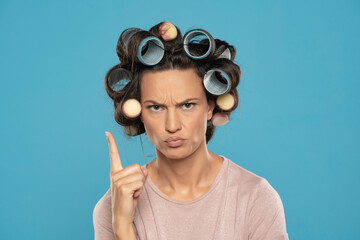 Beautiful angry woman with hair curlers finger pointing on a blue background