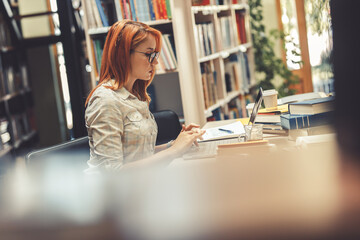 Pretty red hair female student reading a book at the college library.	