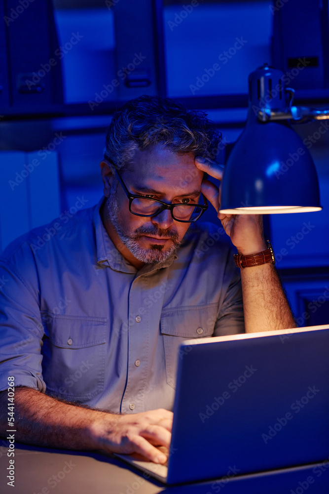 Aufkleber Tired mature male programmer sitting by workplace in front of laptop in office and finding ways of decoding data while working overtime