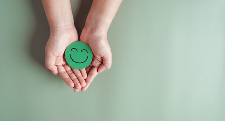 Hands holding green happy smile face, good feedback rating, positive customer review, experience, satisfaction survey, smiley mental health, child wellness, world mental health day on green background