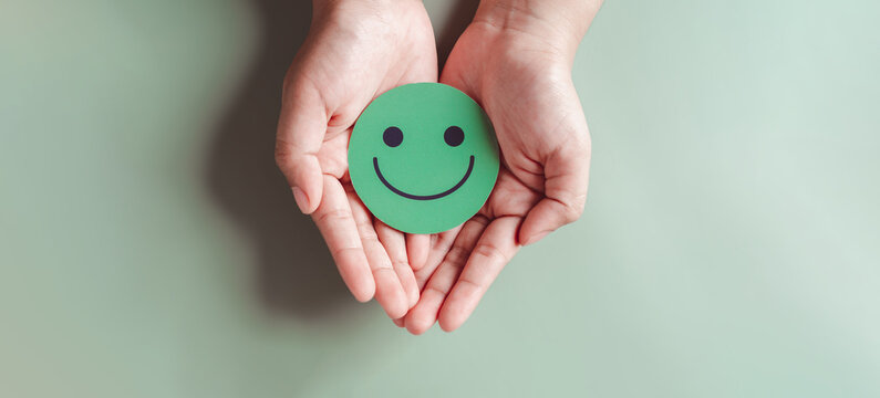 Hands holding green happy smile face, good feedback rating, positive customer review, experience, satisfaction survey, smiley mental health, child wellness, world mental health day on green background