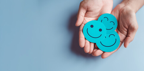 Hands holding blue happy smile face, good feedback rating, positive customer review, experience, satisfaction survey, smiley mental health, child wellness, world mental health day on blue background - obrazy, fototapety, plakaty