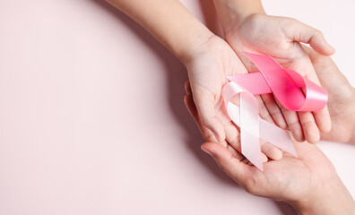 hands of people holding pink ribbons on pink background, Breast cancer awareness, world cancer day, national cancer survivor day in february concept.