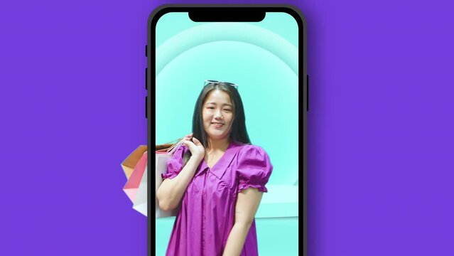 Cheerful young asian woman in dress and eyeglasses standing hold colorful shopping bags in purple color studio background and smartphone. Fashion and shopping concept.