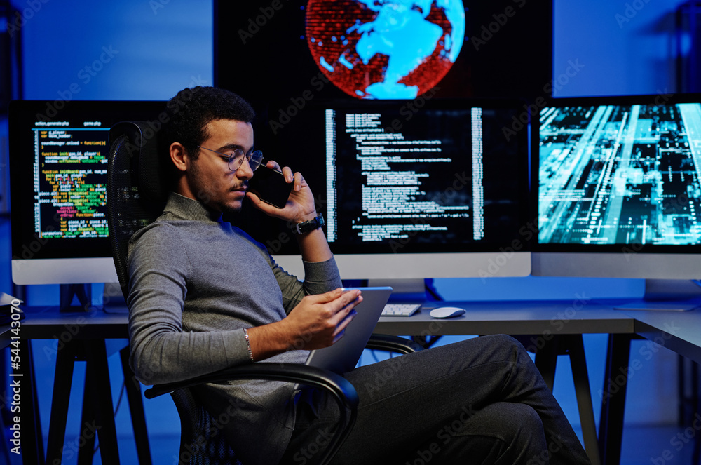 Aufkleber side view of young busy male programmer talking on smartphone and looking through online information
