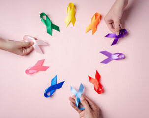 Hands of people holding colorful ribbons on pink background, cancer awareness, World cancer day,...