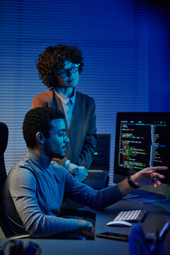 Confident IT engineer or software developer pointing at codes on computer screen while making presentation to female colleague