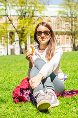 Portrait of happy woman eating bagel at picnic on the grass at sunny day