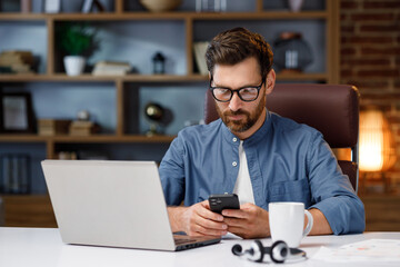 Fototapeta premium Handsome male businessman manager working behind a laptop in a stylish home office. Remote work at home. Portrait of a successful freelancer.