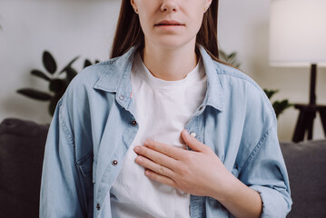 Close-up of upset unhealthy young female sitting on grey sofa at home having reflux acids and pain...