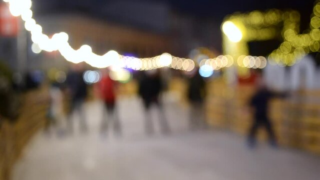Blurred background. Many people skating on open-air ice skating rink, decorated luminous holiday garlands in city on winter evening night. Christmas New Year celebrations holidays recreation backdrop