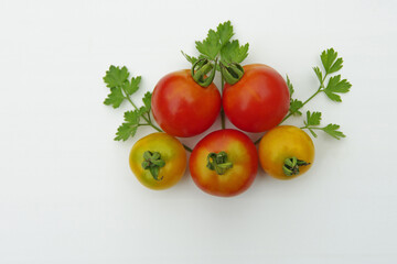 Red and yellow tomatoes with parsley leaves on a white background. Close-up with copy space.