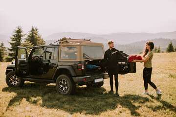 Smiling couple preparing hiking adventure with backpacks by terrain vehicle