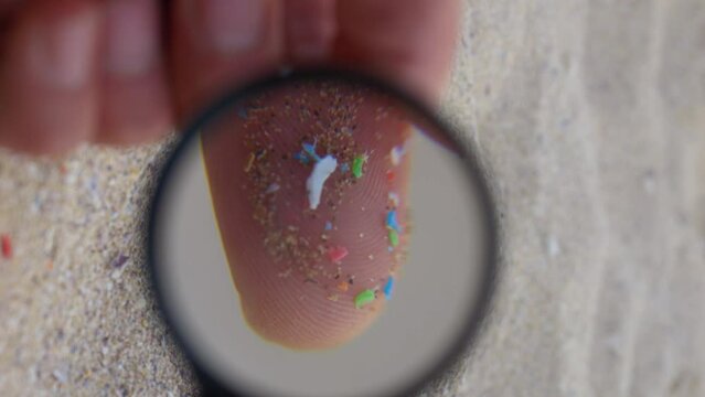 Close up shot of microplastics in hands vertical video. micro plastics in sand. Micro plastics visual identification under a magnifier. Environment, plastic pollution, oceans