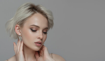 Portrait of a beautiful blonde girl with a short haircut. Gray background.