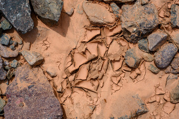 Stones on dried cracked red clay after a landslide in the mountains