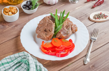 Pieces of boiled beef with fresh vegetables on a white plate on a dark wooden background
