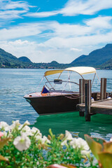 Splendid view of Lake Lugano with the luxury speedboat moored at the shore of Morcote in Switzerland. Beautiful Swiss landscape of the lake and Alps in the background on a sunny summer day.