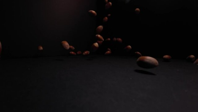 Hazelnuts falling on a black floor and background in 4K slow motion