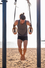 Adult man doing calisthenics exercises on rings outdoors. Sports concept.