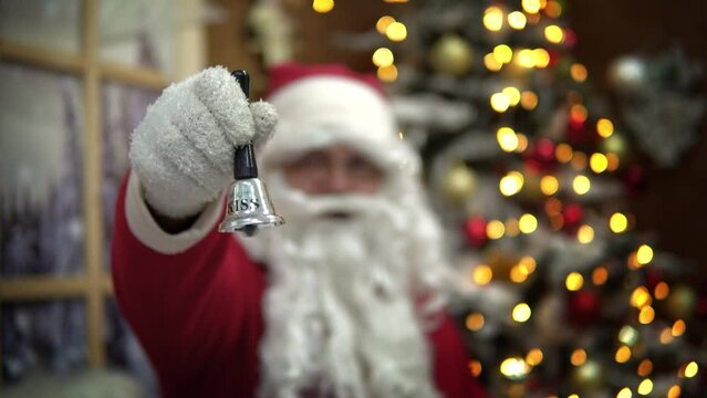 Santa Claus Ringing a Bell with Christmas illuminated tree at background